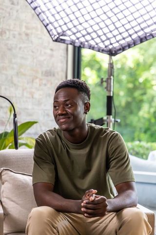 Young man sitting on sofa in home studio lit by softbox, relaxed interview and creator portrait