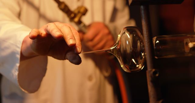 Close-up of glassblower shaping hot molten glass into a sculpture using a blowtorch in a workshop. Ideal for use in articles or advertisements related to artisanal crafts, glassmaking, and creative skills, showcasing the dedication and precision in handmade glass production.