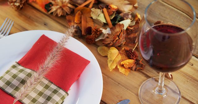 Warm and welcoming table setting using fall-themed decorations, perfect for Thanksgiving or autumn gatherings. This arrangement includes a wine glass filled with red wine, a decorative napkin with a rustic touch, and autumn elements like fallen leaves and pine cones, creating a cozy atmosphere. Ideal for food blogs, seasonal restaurants, and holiday marketing materials.