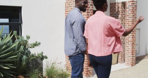 Happy couple holding hands walking towards house on sunny day