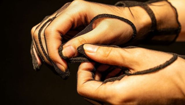 Hands adjusting sheer black mesh gloves showing seams, skin texture and elegant detail