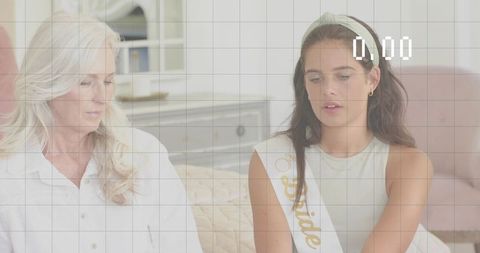 Bride-to-be wearing sash and headband sharing intimate conversation with mother on sofa