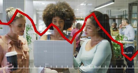 Team collaborating over laptop while analyzing declining financial chart in modern office