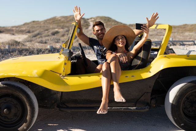 Couple enjoying a sunny day at the beach, sitting in a yellow beach buggy, taking a selfie and waving. Ideal for travel and tourism promotions, summer holiday advertisements, and lifestyle blogs focusing on adventure and romantic getaways.