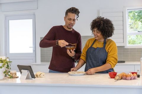 Couple preparing homemade pie together in modern bright kitchen with tablet