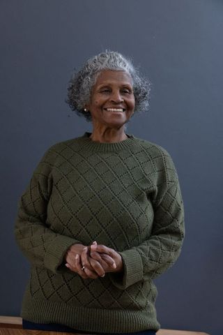 Joyful mature woman in olive green sweater smiling with elegance