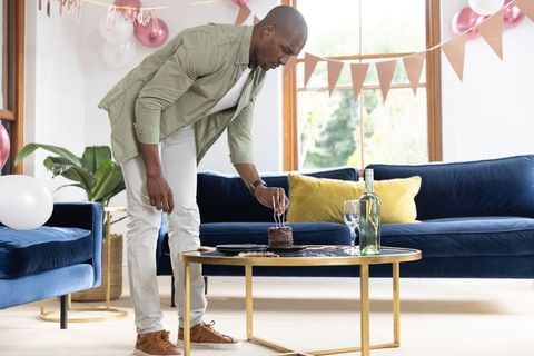 African american man placing birthday candles on chocolate cake in sunlit living room