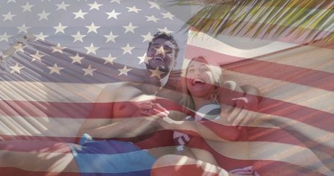 Laughing couple relaxing in hammock under palm with american flag overlay beach getaway
