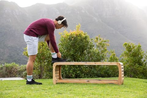 Asian man tying sneaker on bench wearing headphones preparing for run in mountain park