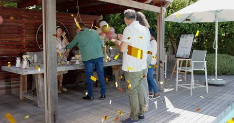Adults celebrating backyard party with cake, confetti and balloons under rustic pergola