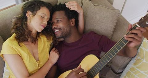 Happy Couple Relaxing on Sofa While Playing Guitar