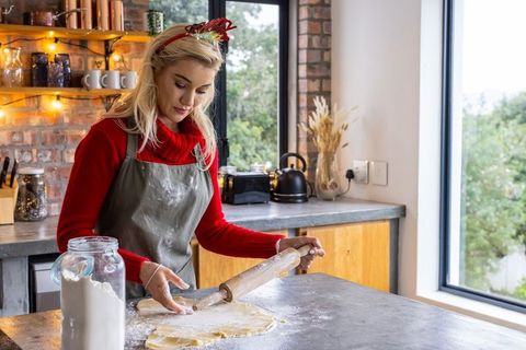 Blonde woman rolling cookie dough in rustic cozy kitchen wearing festive headband