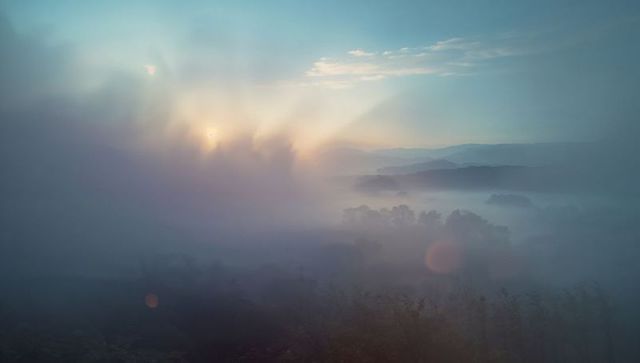 Serene sunrise over misty valley with sunrays piercing fog