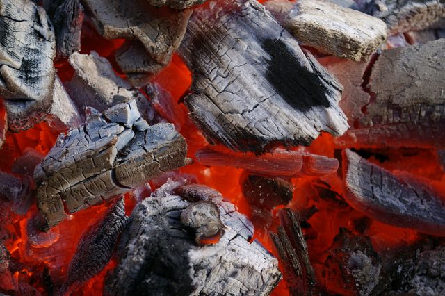 Detailed close-up view of glowing charcoal embers in fire pit. Bright red highlights showcase the intense heat. Suitable for use in articles about barbecuing, camping, or heating. Useful for background images, temperature concepts, and combustion discussions.