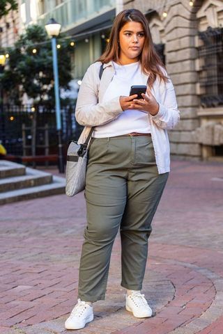 African american woman walking urban plaza using smartphone, casual outfit, city lifestyle