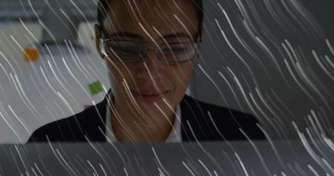 Focused professional woman typing on laptop behind streaked glass with sticky notes