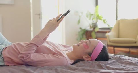 young woman practicing self-care with smartphone and eye patches - Download Free Stock Images Pikwizard.com