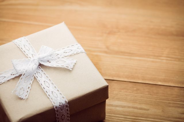Elegant gift box with white lace ribbon on wooden surface. Ideal for use in holiday, birthday, and special occasion promotions. Perfect for blogs, social media posts, and advertisements related to gift giving, celebrations, and packaging.