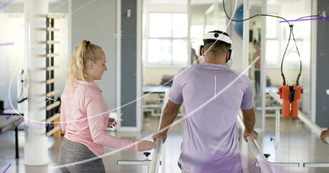 Male Patient Walking on Parallel Bars Guided by Therapist with Orange Harness in Rehab Gym
