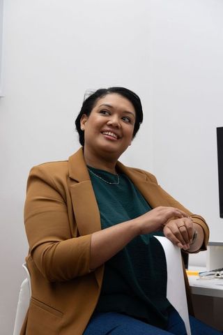 Asian professional woman sitting in office wearing tan blazer and holding paper