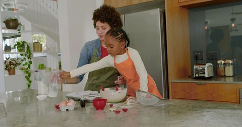 Mother teaching daughter baking in modern kitchen