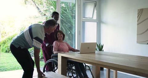 Caregiver Supporting Senior Couple in Wheelchair Chatting at Bright Home