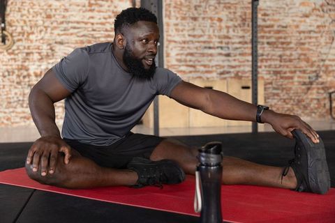 African american athlete stretching hamstring on red mat in industrial gym for mobility