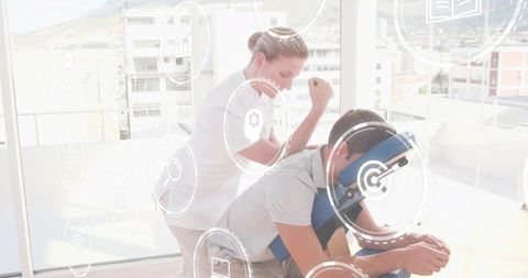 Therapist treating client on blue massage chair in bright clinic with digital wellness icons