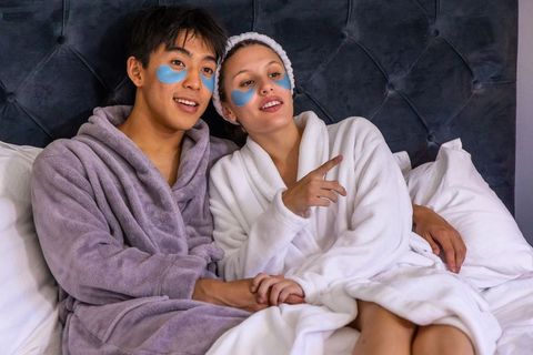 Couple relaxing in bed during cozy at-home spa night with plush robes and eye patches