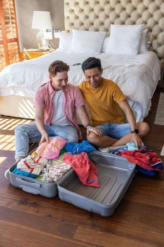 Two male partners packing luggage together in sunny hotel room preparing vacation