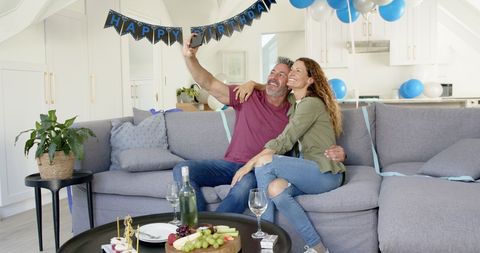 Mature couple sharing joyful birthday selfie on sofa