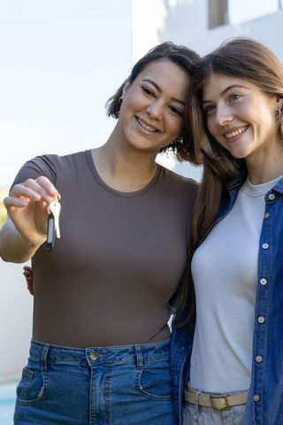 Two women celebrating new homeownership holding keys outdoors