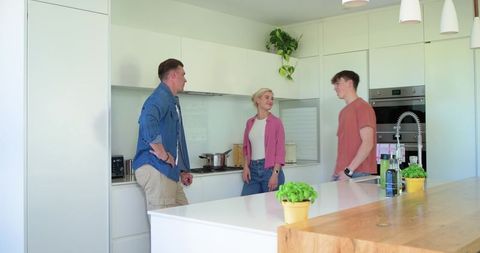 Friends chatting by kitchen island with fresh herb pots in bright modern home