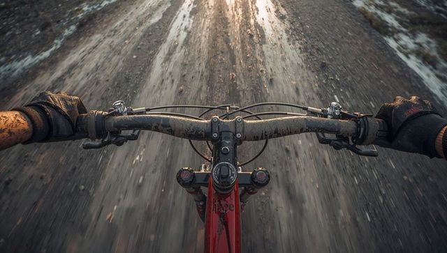 Pov muddy mountain bike crossing wet gravel slush gripping muddy handlebars with brakes