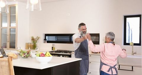 Senior Couple High-Fiving in Contemporary Kitchen During Cooking