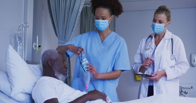 Nurse adjusting oxygen mask for elderly African American patient while doctor observing and noting information on tablet. Suitable for healthcare, patient care, medical services, hospital advertisements, and elder care promotion. Emphasizes teamwork, medical treatment and professional healthcare environment.