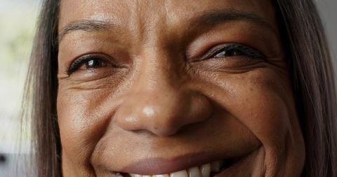 Closeup mature woman smiling broadly with squinted eyes showing upper teeth in soft window light
