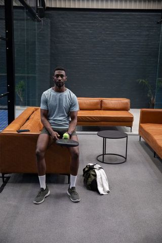 Fit athlete resting on leather sofa holding paddle and ball in modern court lounge