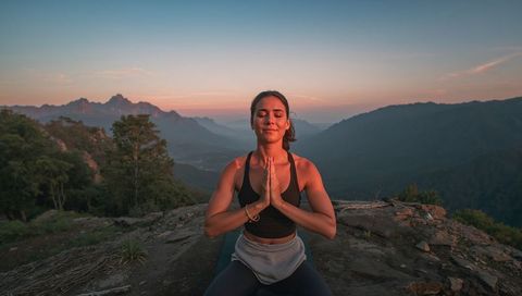 Sunset mountain yoga meditation woman practicing mindfulness on rocky ridge overlook