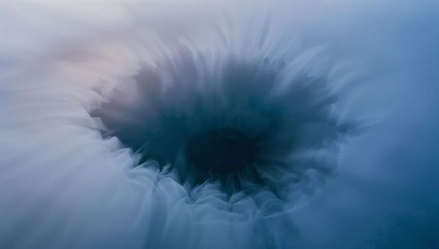 Swirling blue vortex forming on calm water surface with soft gradient ripples