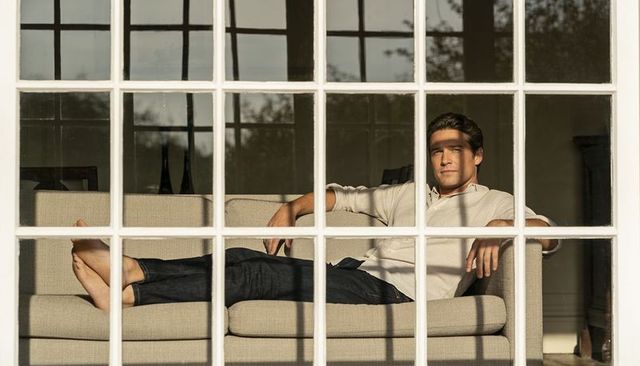 Man reclining on beige sofa basking in sunlight through window panes, casual home lounging