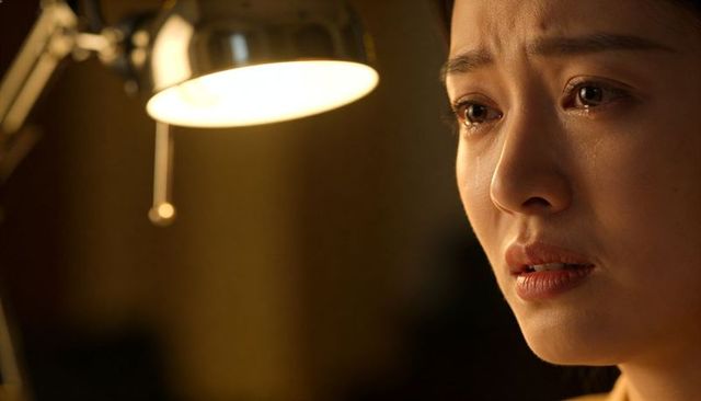 Teary asian woman crying while studying late under desk lamp, emotional closeup, warm lighting