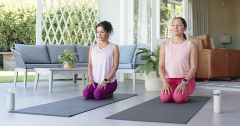Practicing morning patio yoga duo kneeling on mats for mindfulness, wellness, relaxation