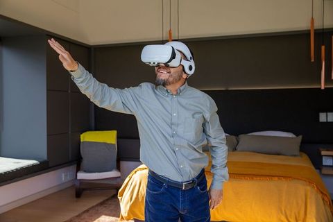 Middle-aged man wearing vr headset in modern bedroom reaching out to interact with virtual world