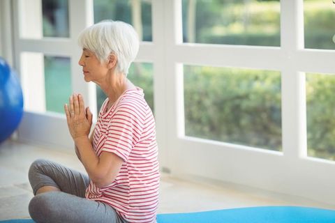 Senior Woman Meditating on Yoga Mat by Large Windows