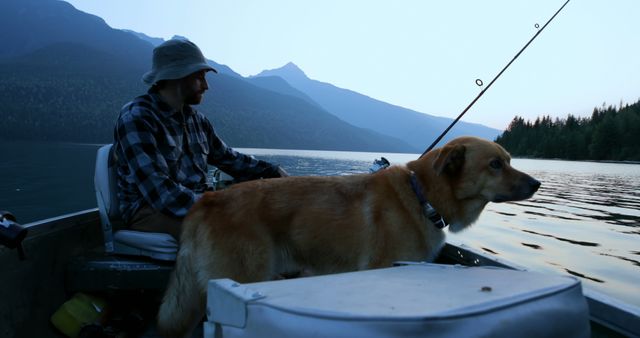 A middle-aged Caucasian man enjoys fishing on a serene lake at dusk, accompanied by his loyal dog, with copy space. Their shared moment highlights the peaceful bond between pet and owner amidst the tranquility of nature.