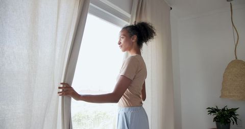 Woman Drawing Curtains in Minimalist Living Room with Natural Light