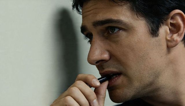 Contemplative man holding pen to lips, closeup profile portrait with shadow, neutral tones