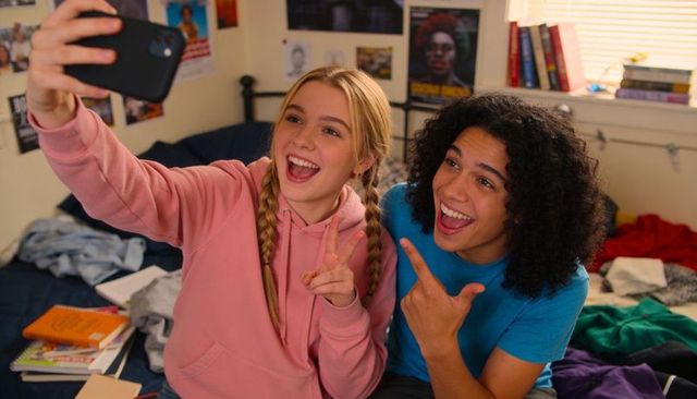 Teen friends taking selfie on unmade bed laughing in casual bedroom moment