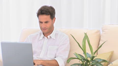 Man Focused on Laptop Relaxing on Sofa with Plant